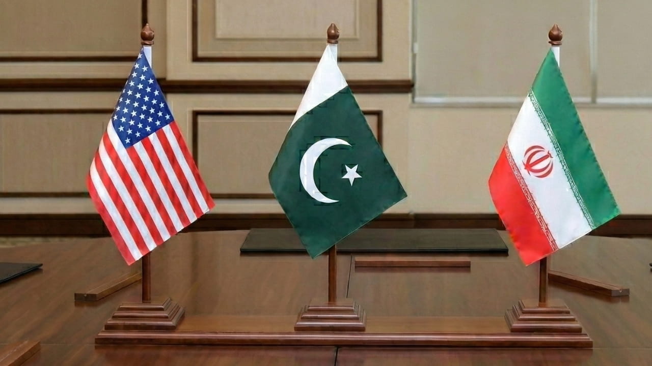 US and Iranian flags on a conference table with Pakistani flag in the center representing peace talks in Islamabad